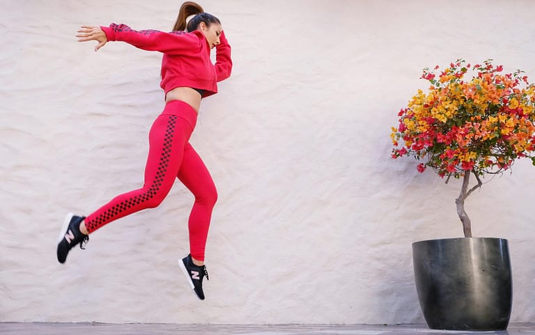 Vibrant woman in red activewear jumping outdoors, epitomizing dynamic fitness and style.